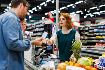 Cashier receiving fidelity card from customer at supermarket checkout