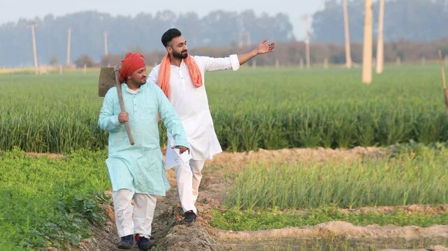 Happy indian farmers walking in Farm land and pointing towards the green lush