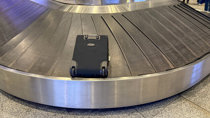 Black suitcase on empty airport baggage carousel, travel logistics, vacation journey, transportation concept © fotoworld