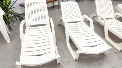 White plastic sun loungers in a row, summer relaxation, outdoor poolside furniture, vacation setting