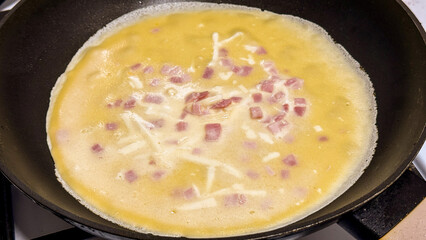 Cooking an omelet with ham and cheese in a skillet, perfect for breakfast, culinary delight