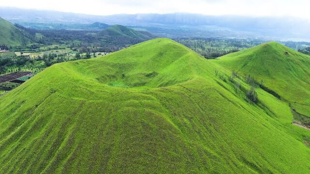 aerial view of green hills peak with grassland and mountain views of Wurung Crater, Indonesia. Aerial shot of the green grassy peak of the mountain crater.