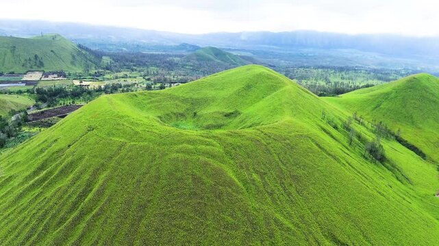 aerial view of green hills peak with grassland and mountain views of Wurung Crater, Indonesia. Aerial shot of the green grassy peak of the mountain crater.