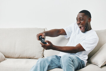 Happy young African American man enthusiastically playing video games on a couch, showcasing...
