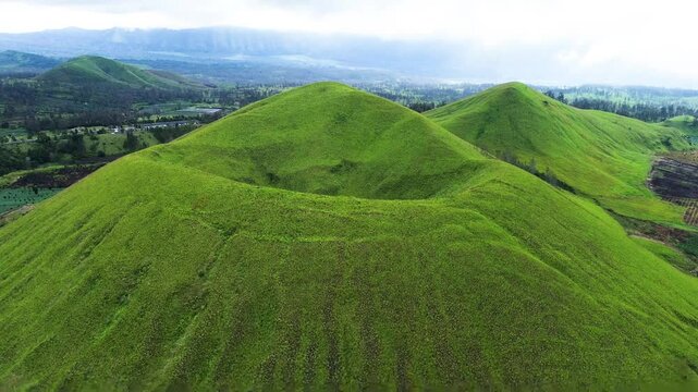 aerial view of green hills peak with grassland and mountain views of Wurung Crater, Indonesia. Aerial shot of the green grassy peak of the mountain crater.
