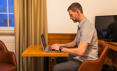 A man sits on a chair in a hotel room and works, relax on his laptop, searching the internet