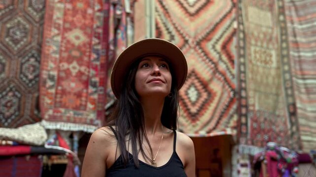 A smiling cowgirl strolls through a tourist shop in Cappadocia, surrounded by ethnic patterned rugs and carpets.The warm glow of lanterns and the region&rsquo;s unique charm enhance the vibrant.