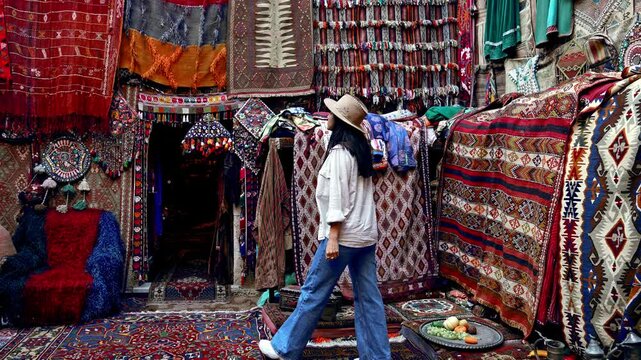 A tourist girl admires the rugs hanging on the wall,appreciating the authentic craftsmanship, ethnic patterns.The warm hues and intricate details reflect the rich culture of G&ouml;reme,Cappadocia.