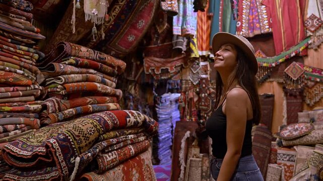 A smiling cowgirl strolls through a tourist shop in Cappadocia, surrounded by ethnic patterned rugs and carpets.The warm glow of lanterns and the region&rsquo;s unique charm enhance the vibrant.