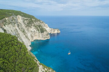 Turquoise waters gently kiss white cliffs as the sun sets over the serene landscapes of Zakynthos. A sailboat glides through the Ionian Sea, revealing hidden gems of this Greek paradise