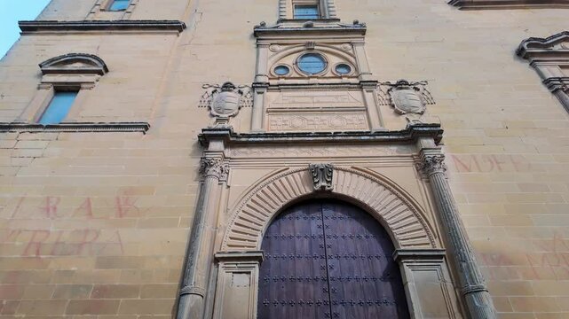 Facade of a medieval church with a large wooden door in the city of Baeza, Andalusia