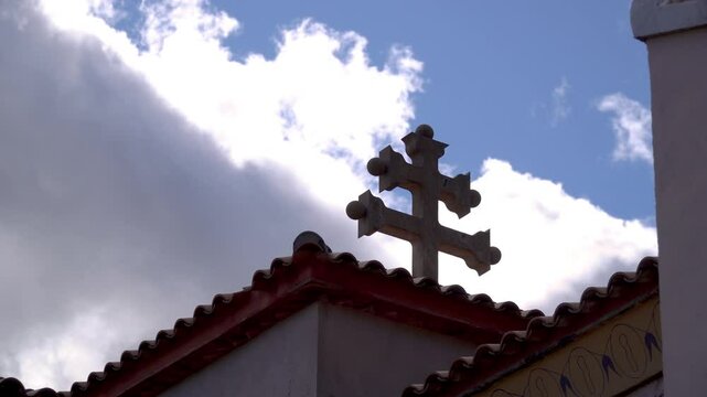 Caravaca cross in the roof of a church, in silhouette against blue cloudy sky.
