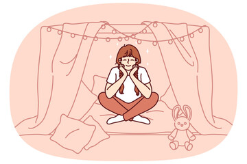 Little girl is sitting in home hut playing children games and dreaming of becoming princess with own castle. School-age girl smiles enjoying exciting game and cozy hut created from sheets and garlands