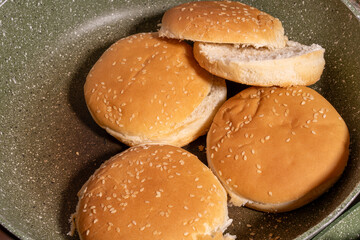 Toasted sesame seed buns arranged in a frying pan, showcasing the preparation of fresh bread for burgers or sandwiches in a homey style.