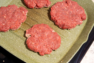 Four raw hamburger patties of ground beef on a ridged green grill pan, perfect for grilling or frying as part of homemade burger preparation.