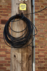 A bundle of wires attached to a wooden pole with a warning sign