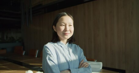 A confident professional woman standing with arms crossed in a modern office, radiating optimism and leadership qualities, with soft lighting enhancing the scene's warmth