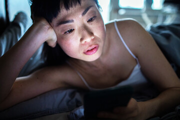 Asian woman lying in bed using smartphone