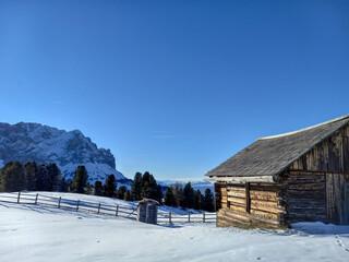 old wooden house in the snowy mountains with a wooden fence and Alps in the background of the ski cabin with a blue sky on a sunny day in the winter