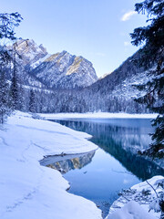 Lake Braies in the winter time in the snowy mountains with a reflection on the crystaline blue water