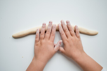 Child hands rolling dough on white surface in baking activity