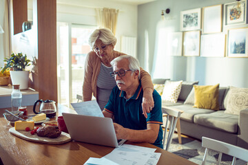 Senior couple managing finances and bills at home with laptop