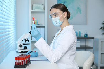Laboratory testing. Doctor holding test tube with blood sample at table indoors