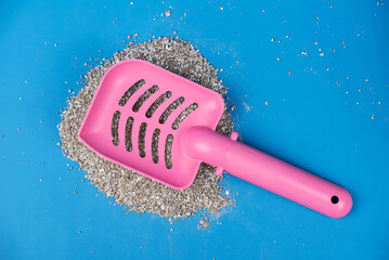 Clumping Cat Litter Scoop on Blue Background. Feline Care Routine: cleaning a cat kitty litter box and adding new absorber granules.