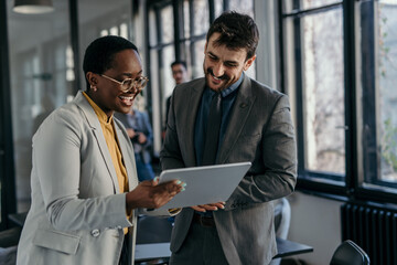 Two business professionals standing in a modern office, collaborating on a tablet