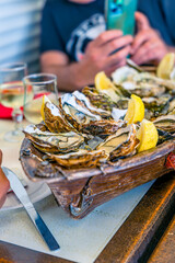 Fresh oysters served on a tray shaped like a fishing boat in a seafood restaurant with a diner taking photos with his mobile phone, in Leucate, France.