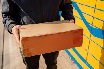 Man Standing with a Parcel Box in Front of Self-Service Lockers &ndash; Waiting to Pick Up or Drop Off a Package. Modern Automated Delivery System, Urban Outdoor Location
