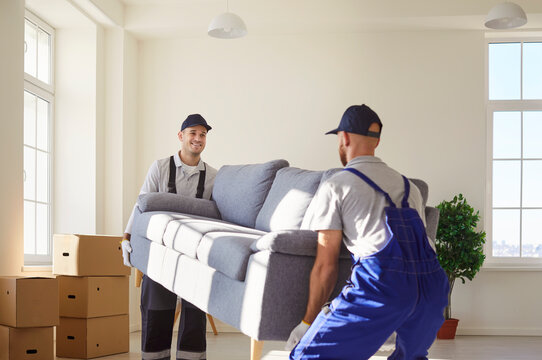 Cheerful man movers carrying a sofa during a relocation to a new home. Moving service staff, teamwork, and the effort involved in transporting furniture for a smooth and efficient move.