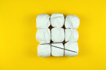 On a yellow background lies white yarn for knitting and knitting needles. Square figure. Business concept