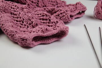 A pink handmade knitted sweater lies on a white background. Knitting needles and a skein of yarn