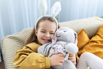 Caucasian child enjoying playtime with plush bunny while wearing bunny ears. Happy Easter