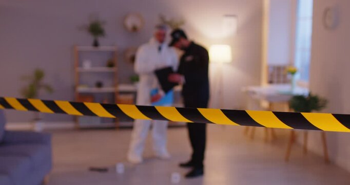 Close-up of police tape at a crime scene where a police officer and criminalist investigate together, searching for evidence. Teamwork emphasizes the importance of collaboration in investigations.