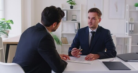 Serious, focused young businessmen signing new contract agreement, skilled lawyer, financial advisor showing place for signature on paper document to male client at meeting in office, agreement deal