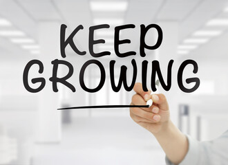 Businessman writing "Keep growing" quote on a transparent wipe board in an office