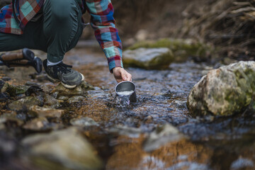 close up on males hands hold and filling a mug with water from creek