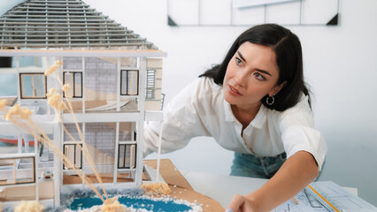 Young beautiful caucasian architect engineer turns house model around to inspect house construction...