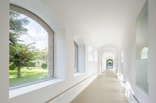 Sunlit corridor of hospital with arched windows overlooking garden