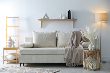 Comfortable sofa with pillows, blanket, lamp and different decor in room. Interior design