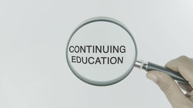 Continuing education text or word highlighted by a magnifying glass in a hand on a white background, symbolizing lifelong learning, skill development, and professional growth