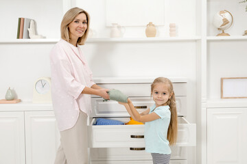 Little girl helping her mother putting clothes into drawers at home