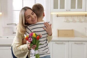 Happy Mother's Day. Son greeting his mom with flowers in kitchen. Space for text