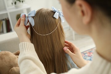 Fototapeta premium Mom putting cute accessories onto her daughter's hair at home, closeup