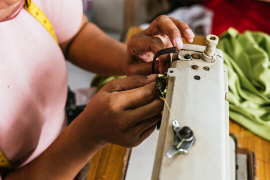 Asian Seamstress Adjusting Industrial Sewing Machine in Workshop