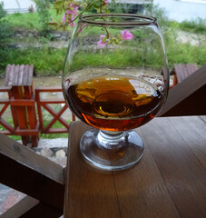 Closeup View Of Glass One Third Filled With Elite Amber Cognac. Vintage Cognac Glass on Wooden Table on Terrace of Private House
