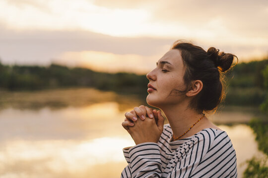 Woman praying at sunset by a tranquil lakeside