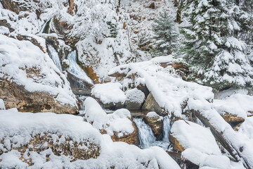 Mountain river in winter, water flows down the riverbed over snow-covered rocks. Winter landscape on a mountain hiking trail.